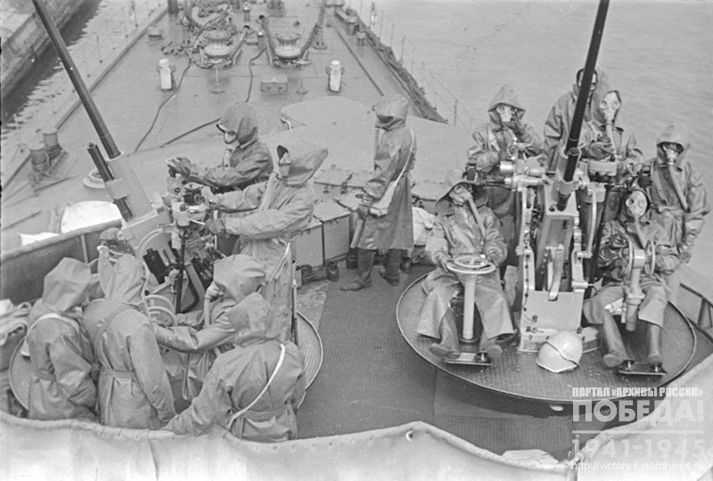 Sailors in gas masks and anti-chemical suits at anti-aircraft guns on the deck of the ship during combat training
