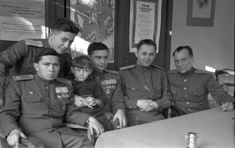 «Заместитель командира 100-го гвардейского истребительного авиационного полка дважды герой Советского Союза майор Д.Б. Глинка в редакции газеты 1-го УФ «За честь Родины». Слева направо: м-р А.П.Верхолетов, к-н С.М.Борзунов, гв. м-р Д.Б.Глинка (с ребенком), редактор газеты п-к С.И.Жуков, спецкор газеты «Сталинский сокол» м-р Н.Н.Бобров.»