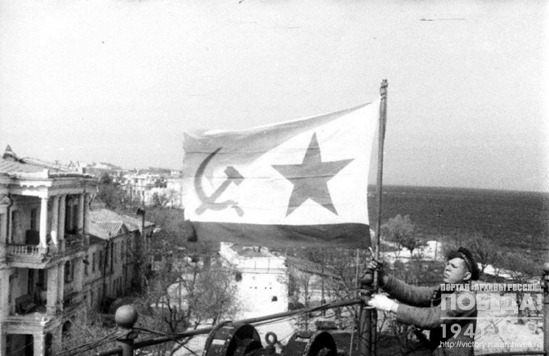 Red Navy men flying a flag over the roof one of the city buildings