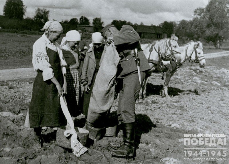 German soldier fills buckets with grain for women who sow