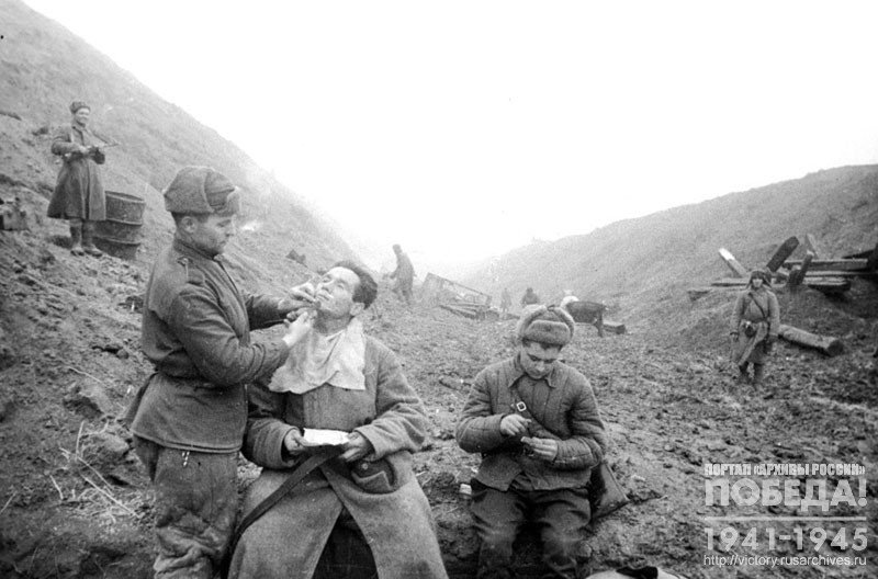 Парикмахер сержант А.Ф. Халабузарь бреет командира минометного взвода лейтенанта Д.И. Симулина