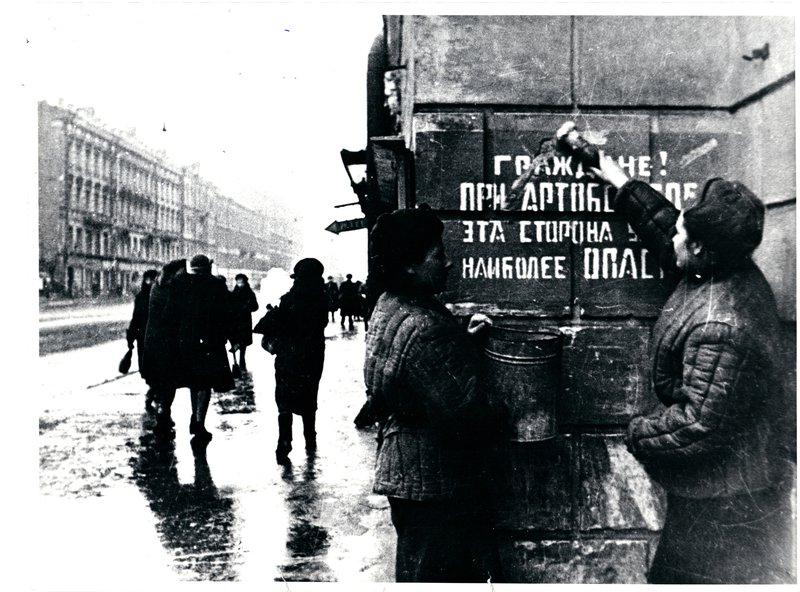 After breaking the blockade people cover up the inscription on the wall saying about danger of artillery shelling in front of the Lensovet theatre