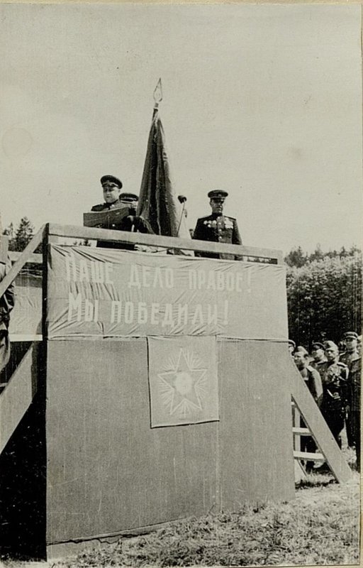 Фотография: Член Военного Совета 31 армии Генерал-Майор Карпенков зачитывает указ Президиума Верховного Совета Союза ССР о вручении боевого Красного Знамени дивизии. Справа - командир 36 стрелкового Неманского Краснознаменного корпуса Герой Советского Союза Генерал-Майор Провалов