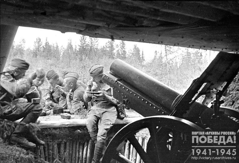 Бойцы гаубичной батареи за обедом у своего орудия на передовой Ленинградского фронта