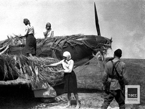 Мирные жители во время маскировки советского военного самолета на полевом аэродроме