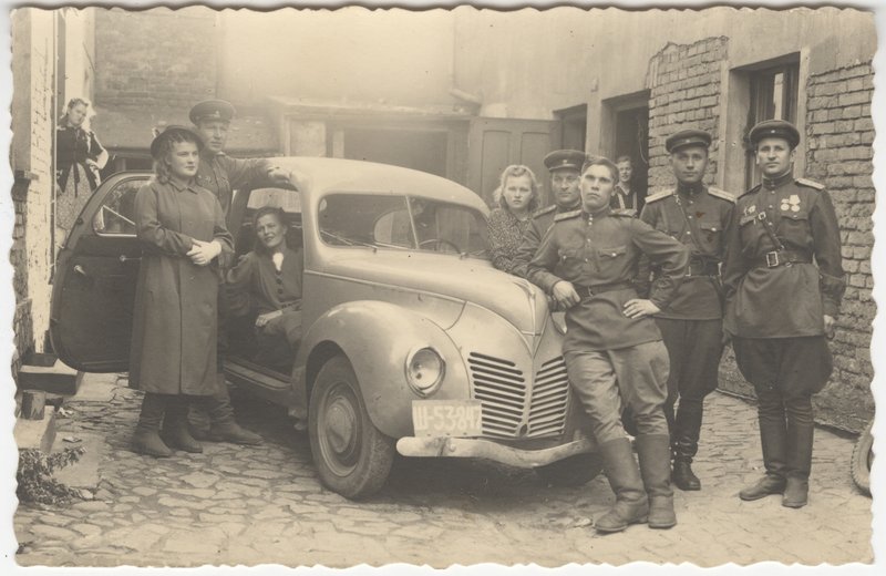 "Group of officers with ladies by a passenger car."