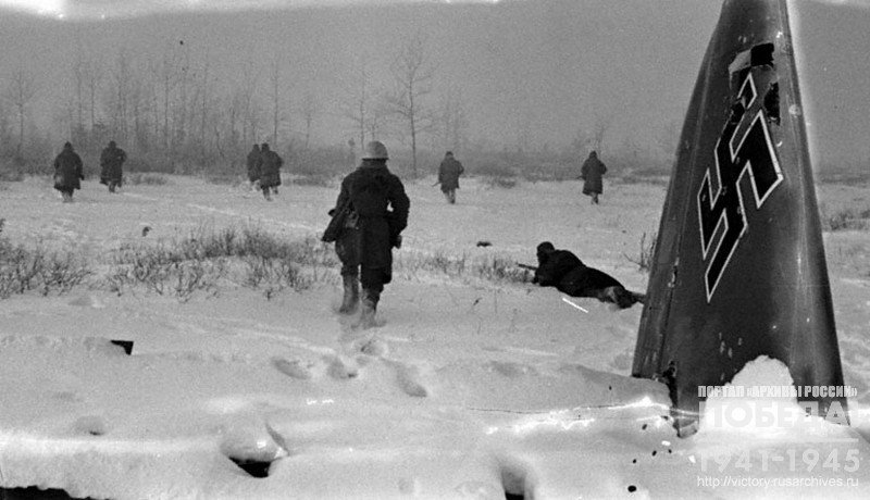 Soldiers attacking field woodland occupied by Germans. Front and center -   downed German airplane wrecks