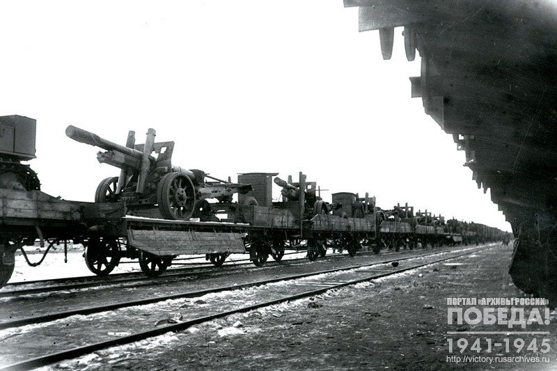 Train with artillery pieces, heading to the front, at one of the railway stations